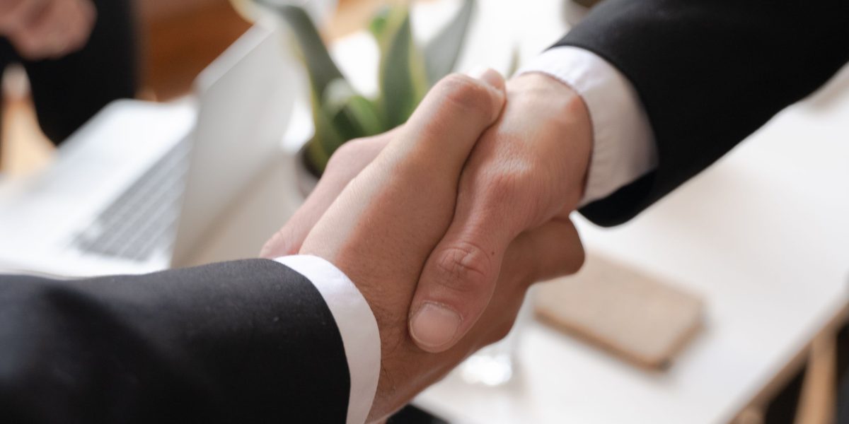 Two professionals shaking hands in a modern office setting, representing the successful formation of a partnership or investment deal.